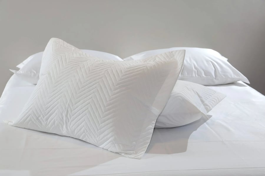 Porta-travesseiro branco CIÇA com matelassado em zigzag sobre a cama